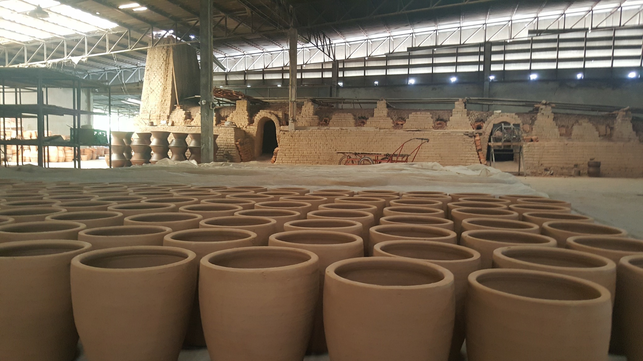 Handmade terracotta planters drying in a Thai pottery workshop with traditional kilns